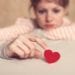 Sad girl is holding heart symbol by her finger and looking at it. Love and relationships concept