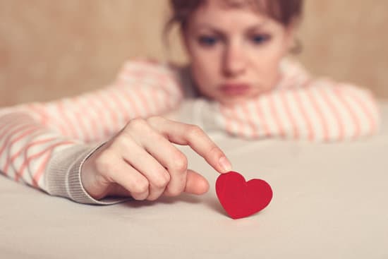 Sad girl is holding heart symbol by her finger and looking at it. Love and relationships concept