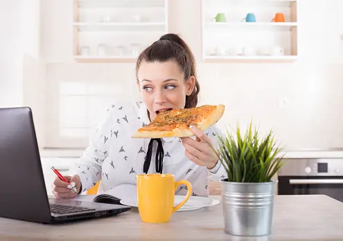 Busy young business woman eating pizza and looking at laptop. Working from home