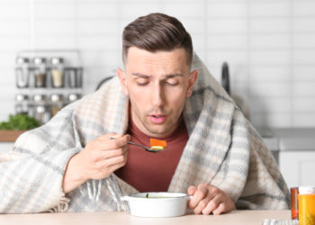 Sick young man eating broth to cure cold at table in kitchen; Shutterstock ID 1095168275; Job: GSK