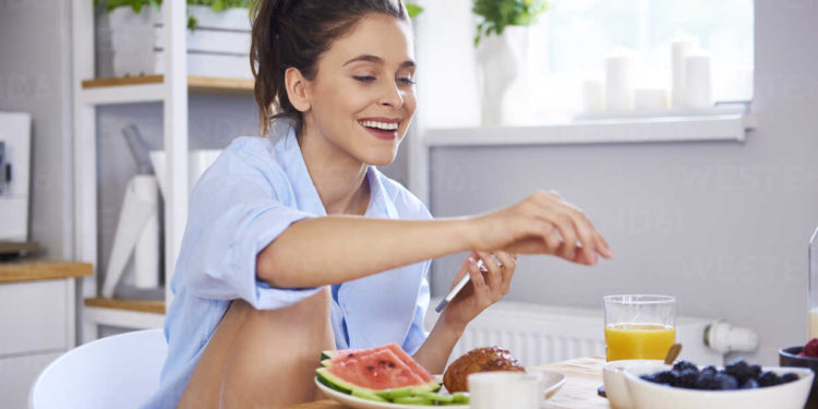 Young woman at home in kitchen, eating breakfast