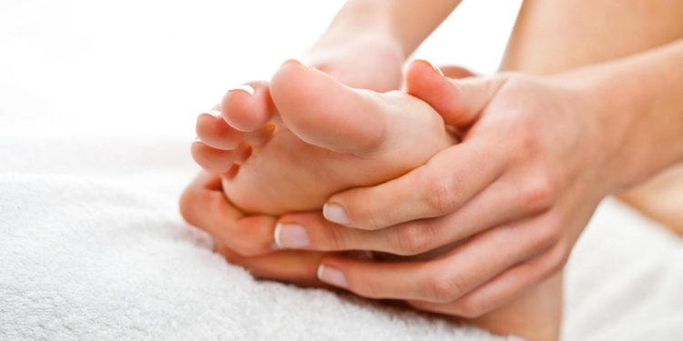 Woman making foot massage holding her foot with both hands on the white towel.r