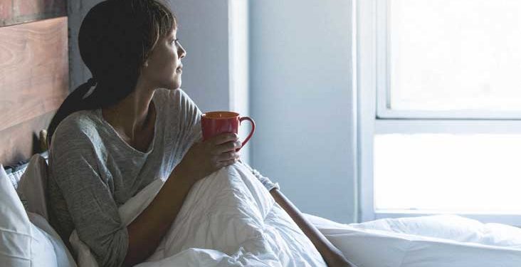 millennial African-American woman spending her morning in her bed, in her pajamas, with a warm mug of coffee, staring out the windown day dreaming or happily thinking to herself.
675090804