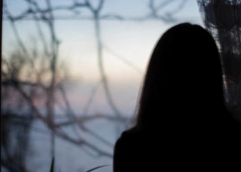 Silhouette of a girl on a background of a dark window in the house - depression, reflection, danger, blur