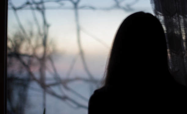 Silhouette of a girl on a background of a dark window in the house - depression, reflection, danger, blur