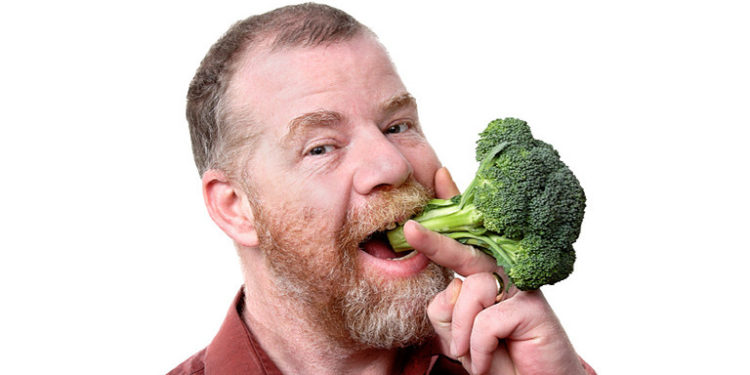A man holds a piece of broccoli to his mouth.