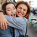 Close-up photo of laughing woman friends hugging each other on city street