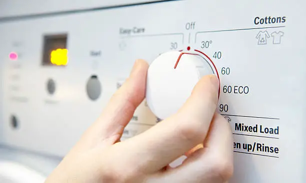 Woman Selecting Cooler Temperature On Washing Machine To Save Energy