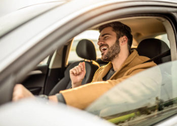 Photo of cheerful young man driving a car and singing.