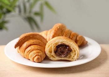 Plate of fresh croissants with chocolate stuffing on wooden table indoors, closeup. French pastry