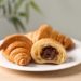 Plate of fresh croissants with chocolate stuffing on wooden table indoors, closeup. French pastry