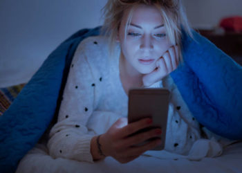 Disappointed sad woman holding mobile phone while laying on bed at night