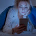 Disappointed sad woman holding mobile phone while laying on bed at night